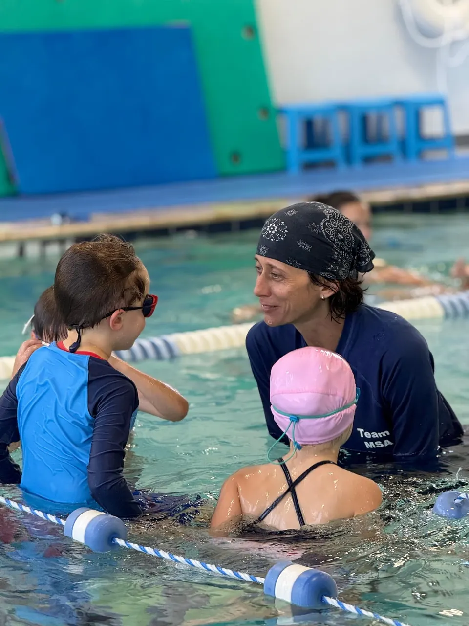 A coach at the pool edge working with two children in the water