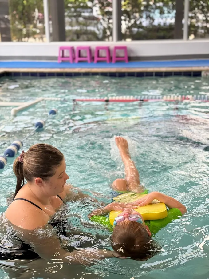 A child gliding on her back over a yellow kickboard while the instructor steadies her